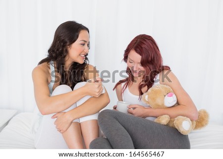Relaxed young female friends chatting over coffee in bed at home