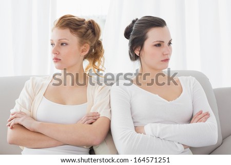 Unhappy young female friends not talking after argument at home on the couch