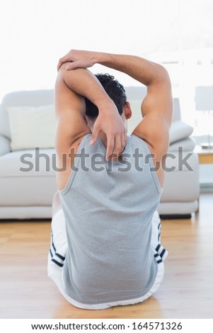 Rear view of a sporty young man stretching hands behind back in the living room at house