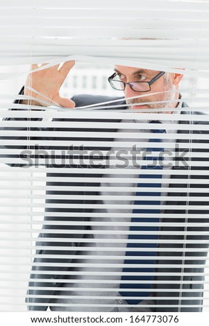 Close-up of a serious mature businessman peeking through blinds in the office