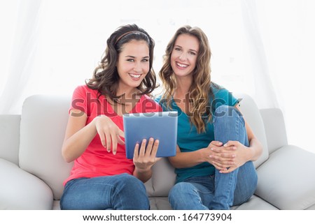 Portrait of two smiling young female friends using digital tablet in the living room at home