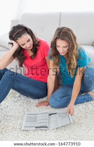 High angle view of two young female friends reading a book in the living room at home