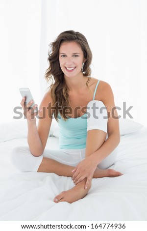 Portrait of a smiling young woman sitting with mobile phone in bed at home