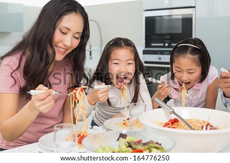 Woman With Her Two Happy Kids Enjoying Spaghetti Lunch In The Kitchen At Home