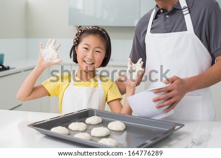Portrait of a cheerful girl with her father preparing cookies in the kitchen at home