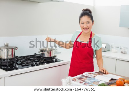 Portrait of a smiling young woman with recipe book preparing food in the kitchen at home