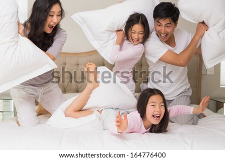 Cheerful Kids And Parents Having Pillow Fight On Bed At Home