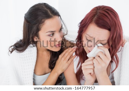 Young Woman Consoling A Crying Female Friend While Sitting On Bed At Home