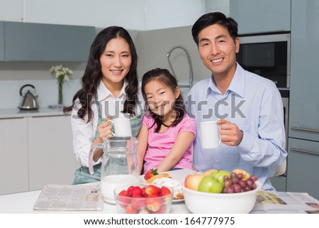 Portrait of a happy young girl enjoying breakfast with parents at table in the kitchen