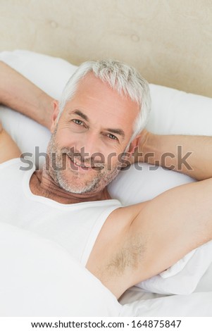 High angle portrait of a smiling mature man resting in bed at home