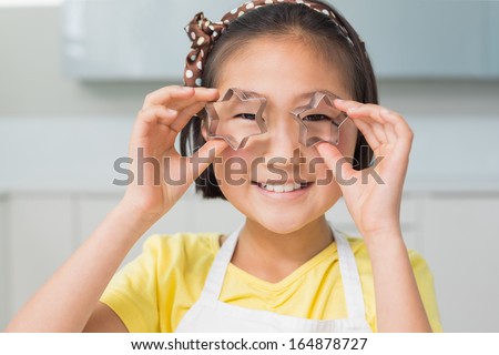 Close-up portrait of a smiling young girl holding cookie molds in the kitchen at home