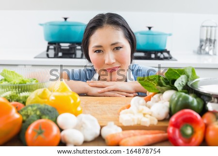 Portrait of a smiling young woman in front of vegetables in the kitchen at home