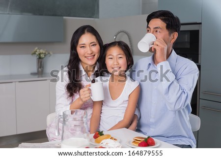 Portrait of a happy young girl enjoying breakfast with parents at table in the house