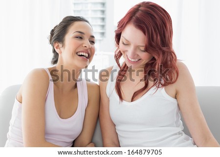 Two beautiful young female friends laughing in the living room at home