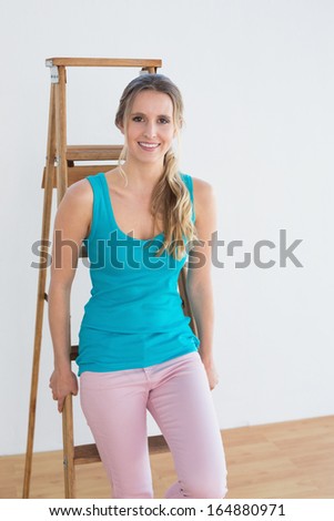 Portrait of a happy young woman standing against ladder in a new house