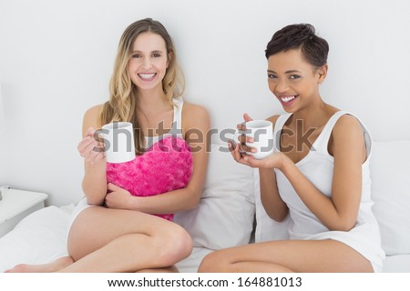Portrait of young female friends with coffee cups in bed at home