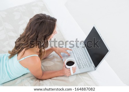 High angle view of a relaxed young woman using laptop with coffee cup in bed at home