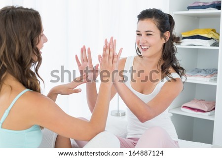 Happy young female friends playing clapping game at home