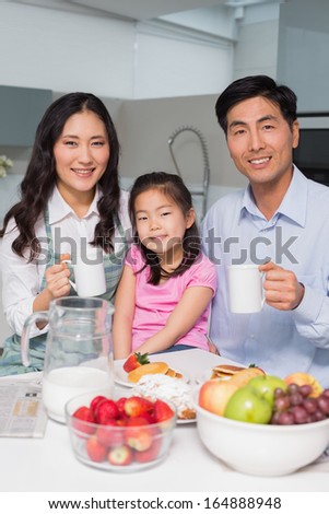 Portrait of a happy young girl enjoying breakfast with parents at table in the kitchen