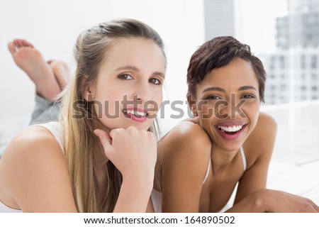 Portrait of two smiling young female friends lying in bed at home