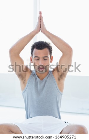 Close-up of a young man meditating with eyes closed and joined hands against bright background