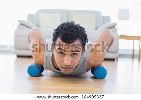 Portrait of a sporty young man with dumbbells doing push ups in the living room at house