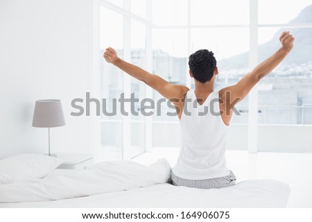 Rear view of a young man waking up in bed and stretching his arms Rear view of a young man waking up in bed and stretching his arms