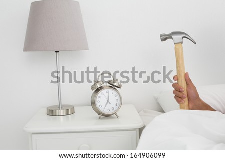 Close-up of a man\'s hand smashing alarm clock with hammer in bed at home