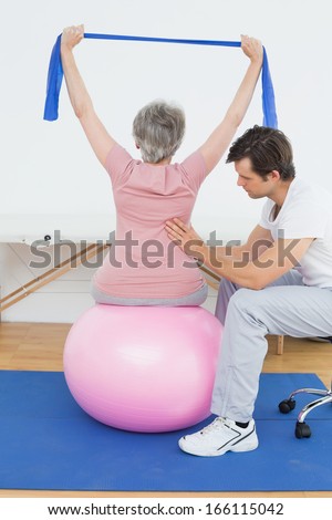 Senior woman sitting on yoga ball while working with a physical therapist
