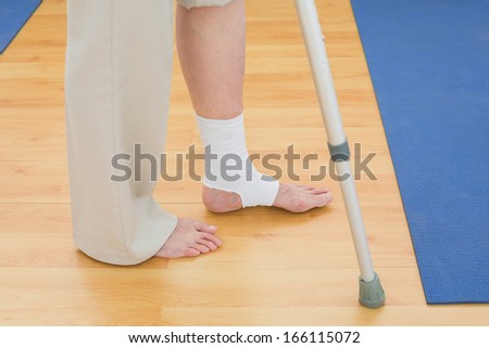 Close-up low section of a woman with crutch and bandaged leg in the hospital gym