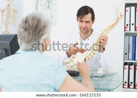 Male doctor explaining the spine to a senior patient in medical office