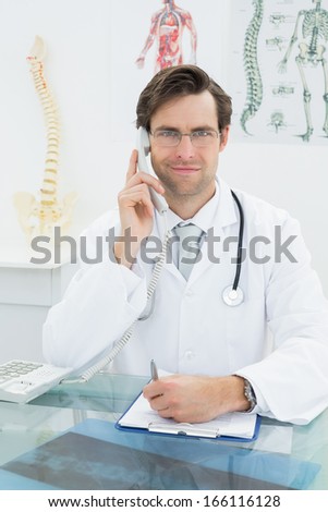 Portrait of a smiling young male doctor using telephone at the medical office