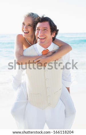 Happy bride getting a piggy back from handsome husband at the beach