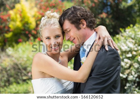 Husband hugging his new wife smiling at camera in the countryside