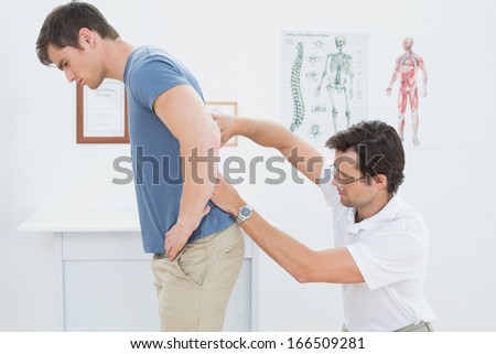 Side view of a male physiotherapist examining mans back in the medical office