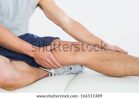 Close-up mid section of a man with his hands on a painful leg