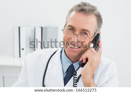 Close-up portrait of a smiling male doctor using telephone at the medical office