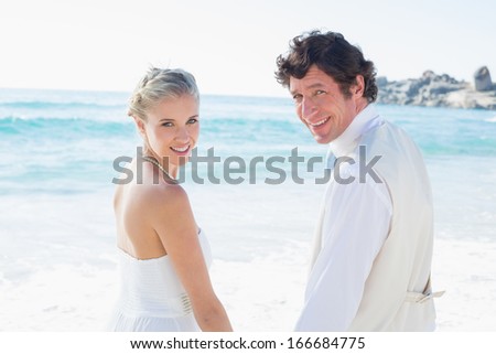 Bride and groom holding hands smiling at the camera at the beach