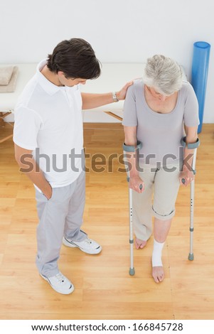 Male therapist assisting disabled senior patient to walk in the gym at hospital