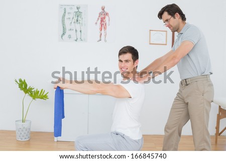 Side view of a male therapist assisting young man with exercises in the medical office