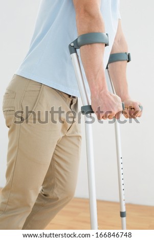 Side view mid section of a man with crutches standing indoors