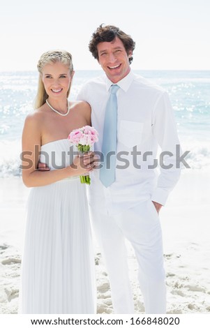 Cute happy couple on their wedding day smiling at camera at the beach