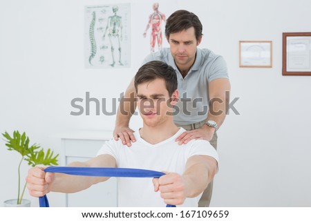 Male therapist assisting young man with exercises in the medical office