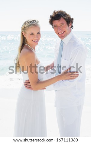 Romantic happy couple on their wedding day smiling at camera at the beach