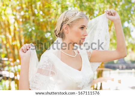 Content blonde bride holding her veil out in the countryside
