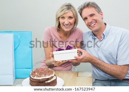 Man giving a happy woman a birthday gift beside cake and shopping bags at home