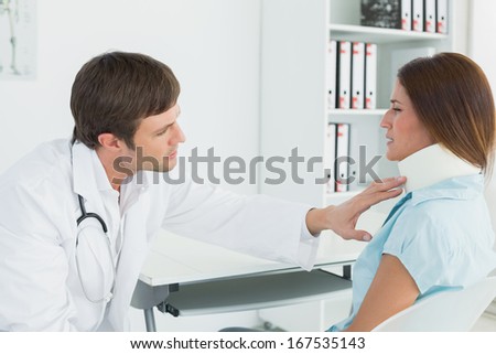 Side view of a male doctor examining a patient\'s neck at desk in medical office