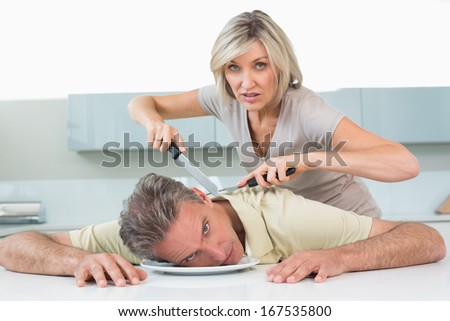 Angry woman holding knife to man\'s neck in the kitchen at home