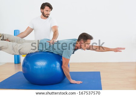 Physical therapist assisting young man with yoga ball in the gym at hospital
