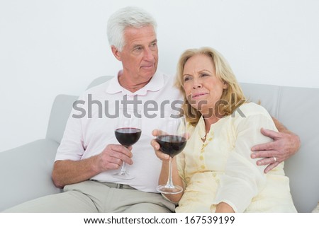 Relaxed senior couple with wine glasses sitting on sofa at home